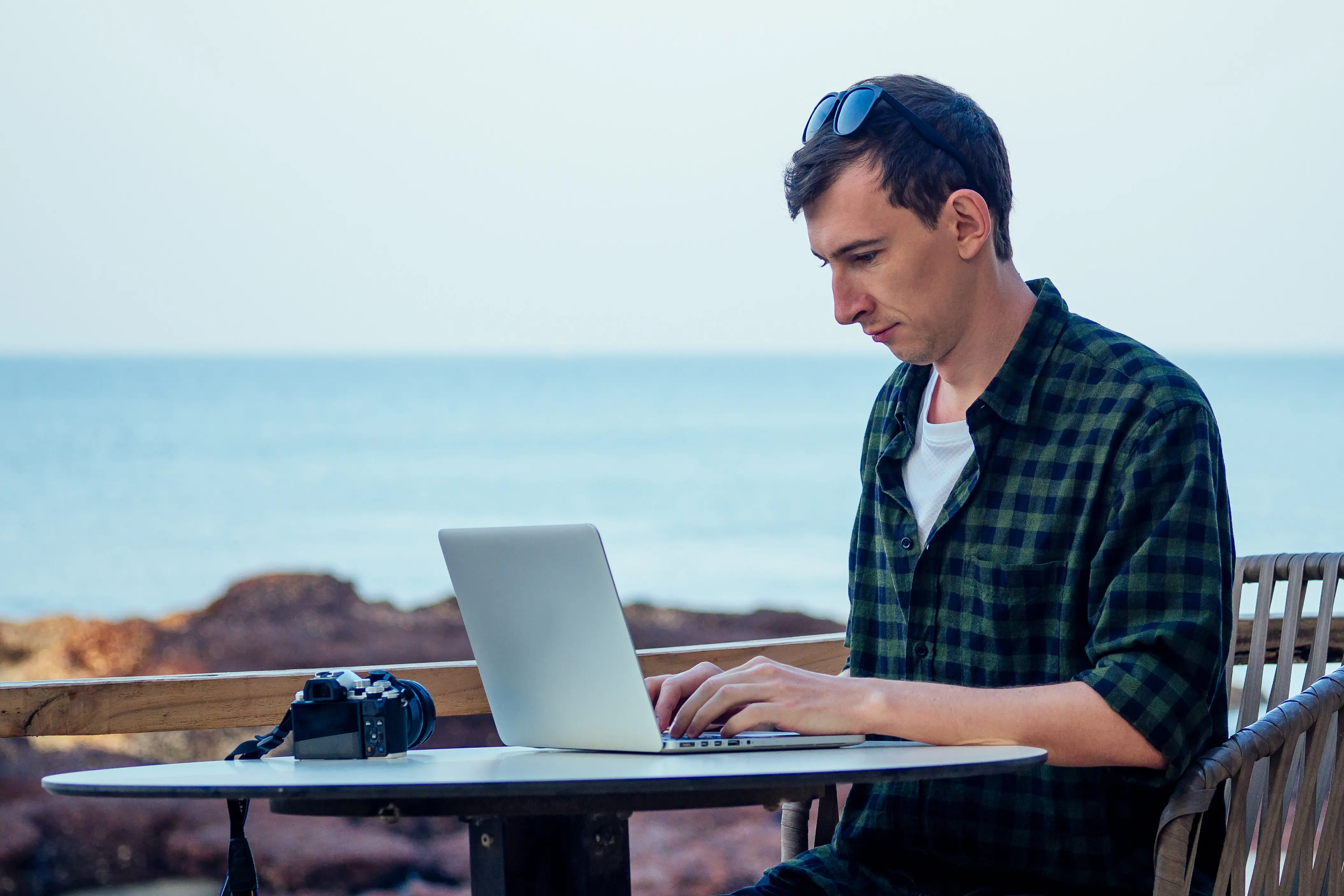 Fernarbeit, Surfen und Freiberufler-Urlaub: Ein junger freiberuflicher Surfer und Geschäftsmann arbeitet mit dem Laptop an einem tropischen Strand, im Sommercafé auf der Straßenveranda, im Urlaub in einem exotischen Land.