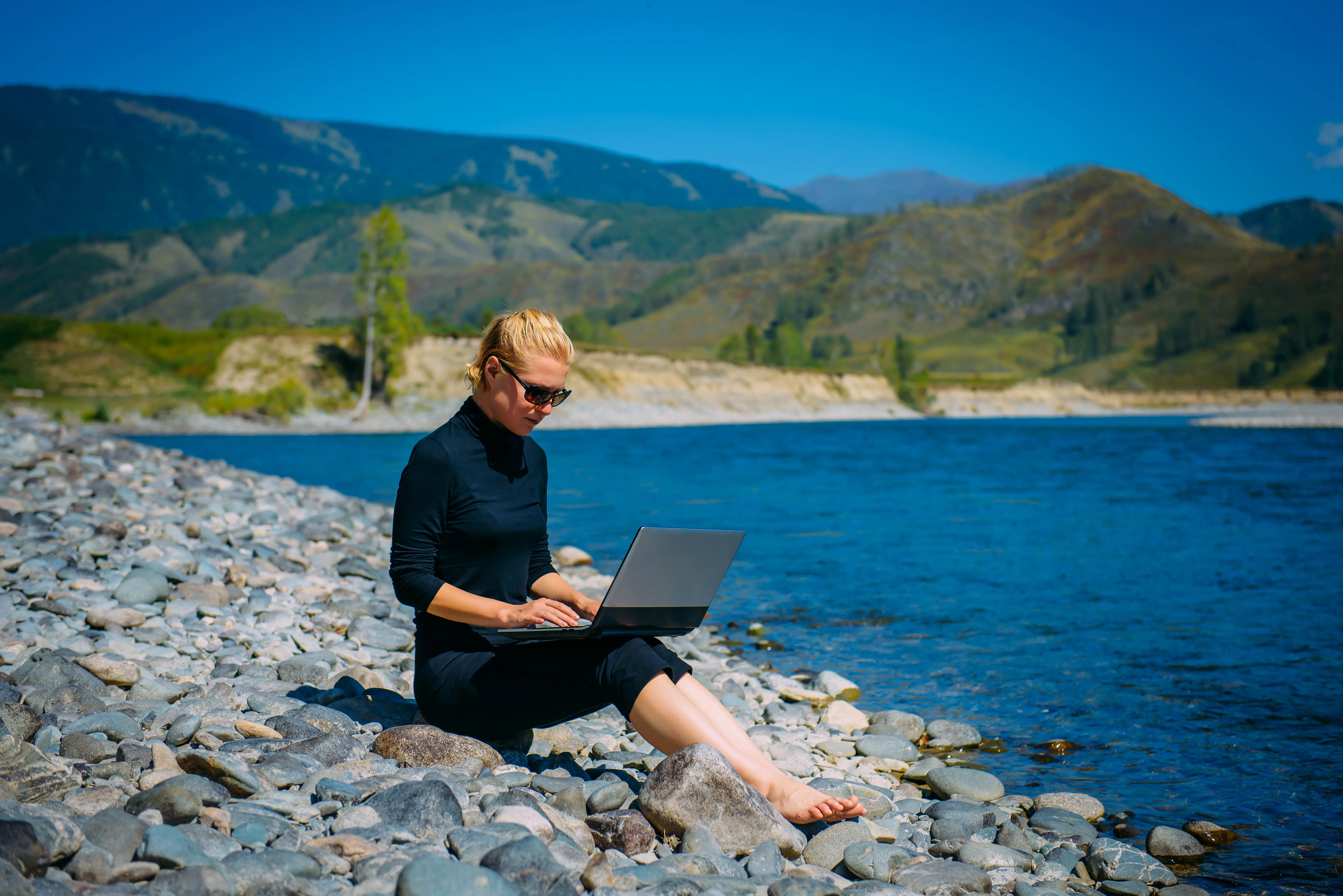 Eine Frau sitzt auf Felsen und benutzt einen Laptop.