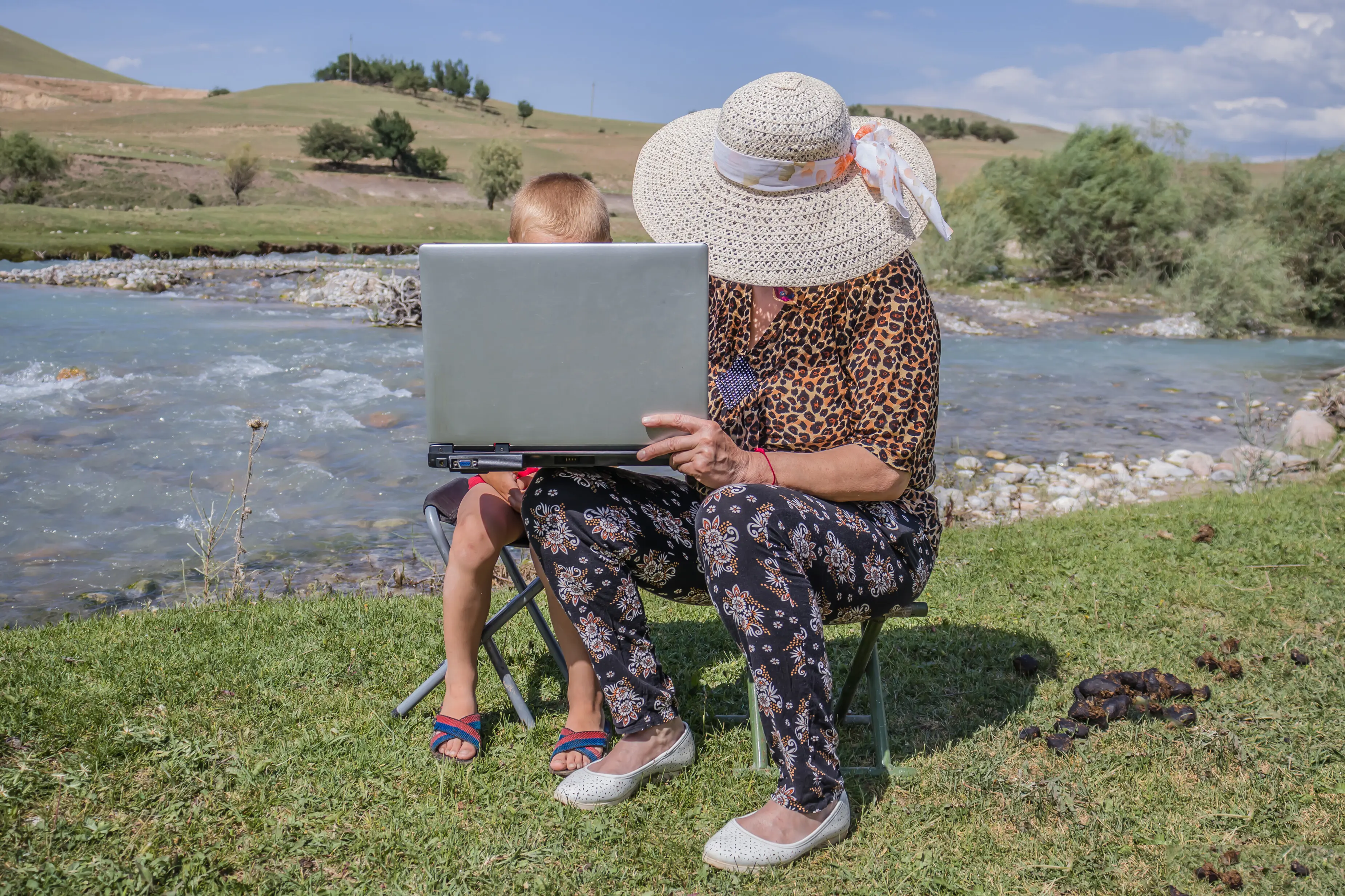Großmutter und Enkel am Computer am Flussufer; Fernunterricht von Schulkindern.