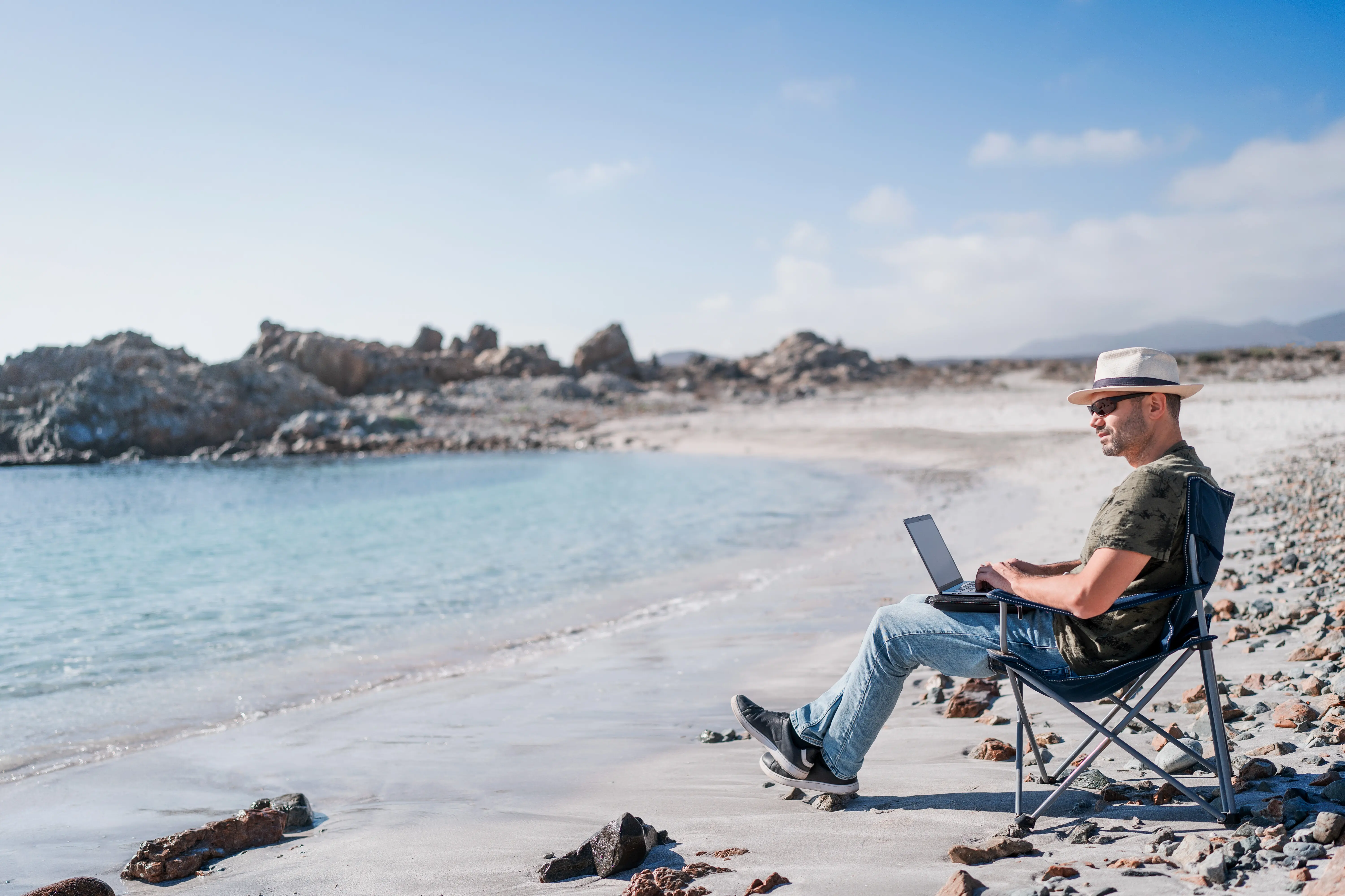 Ein digitaler Nomade sitzt allein am Strandufer und arbeitet entspannt.